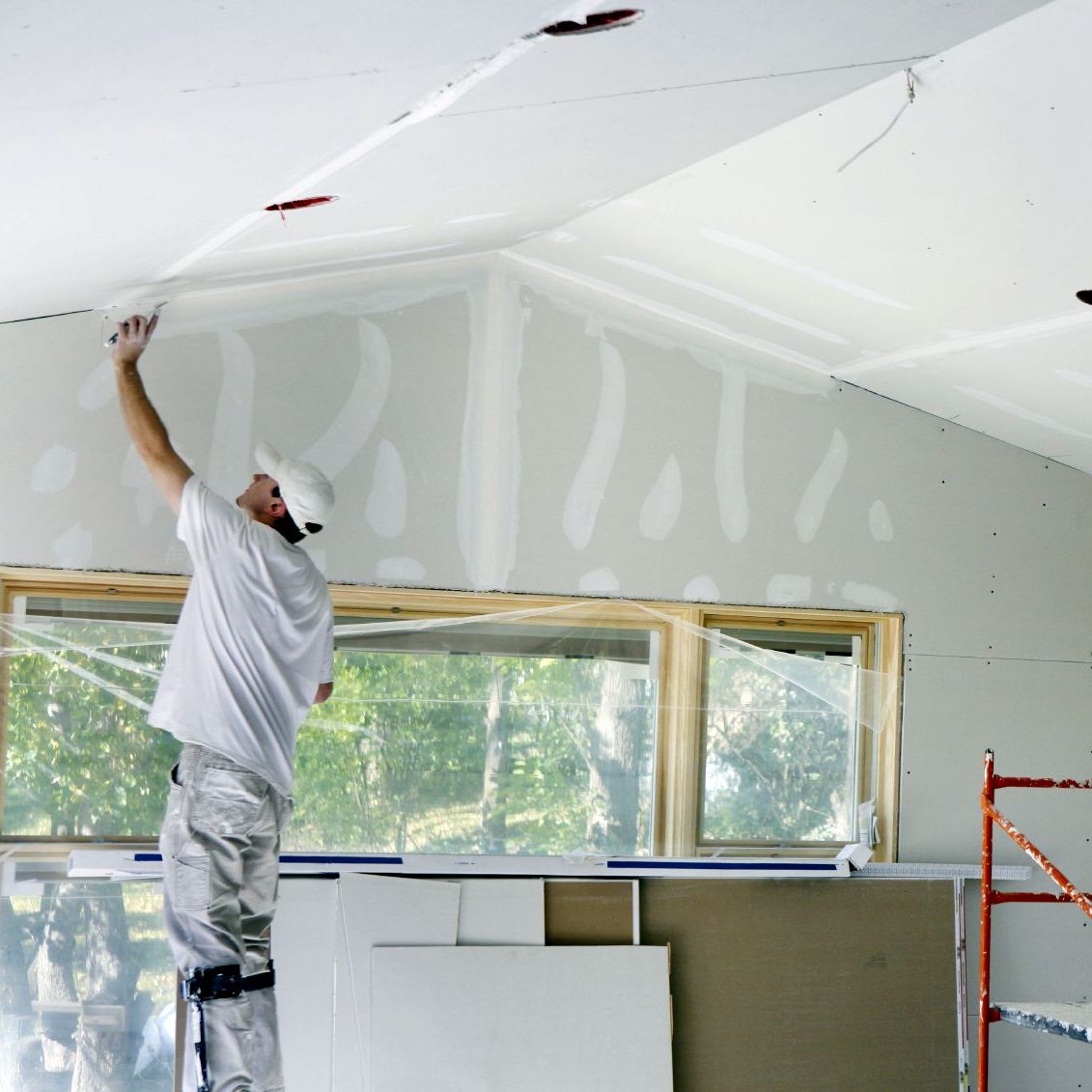 Maliar upravuje sadrokartónový strop pred maľovaním. Maľovanie sadrokartónového stropu je náročné, nie každý ho zvládne.